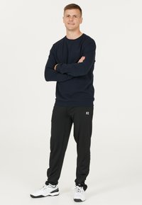 Marinblå sweatshirt med rund hals och FZ-logotyp, ihop med svarta träningsbyxor med avsmalnande ben och vita träningsskor.