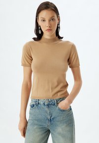 Beige kortærmet strikket top med høj hals, der har ribbede manchetter og kant. Kombineret med lyseblå højtaljede tapered jeans.