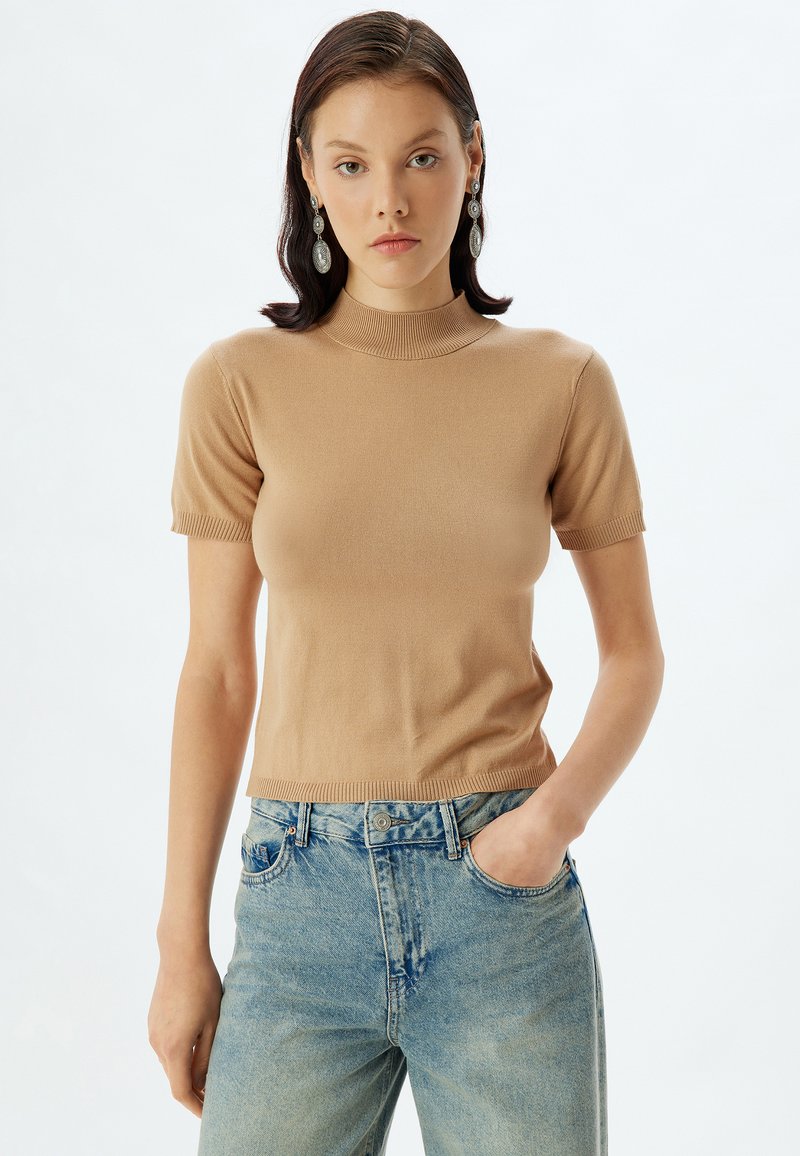 Beige kortærmet strikket top med høj hals, der har ribbede manchetter og kant. Kombineret med lyseblå højtaljede tapered jeans.