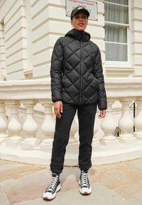 Sort dunjakke med diamantquiltning, høj krave og lynlås. Parret med sorte sweatpants og høje sneakers.