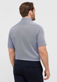 Camicia a maniche corte in un motivo geometrico blu e bianco, con colletto classico e tessuto morbido. La vista posteriore mostra un design semplice.