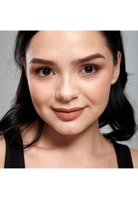 Primo piano di un volto con pelle liscia, capelli scuri e rossetto opaco in tonalità neutra. Le caratteristiche includono sopracciglia definite e occhi scuri ed espressivi.