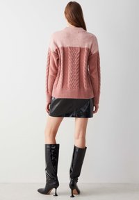 Chunky pink sweater with cable knit detailing, paired with a glossy black leather mini skirt and knee-high pointed boots.