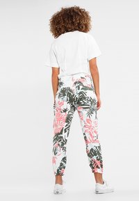 Färgglada byxor med blommönster som har gröna och rosa löv på en vit bakgrund, med en avslappnad passform och elastiska muddar vid anklarna.