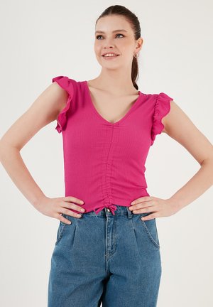 Haut rose côtelé avec de courtes manches volantes et un col en V. Comprend des détails froncés au centre et un lien à l'ourlet, associé à un jean bleu.