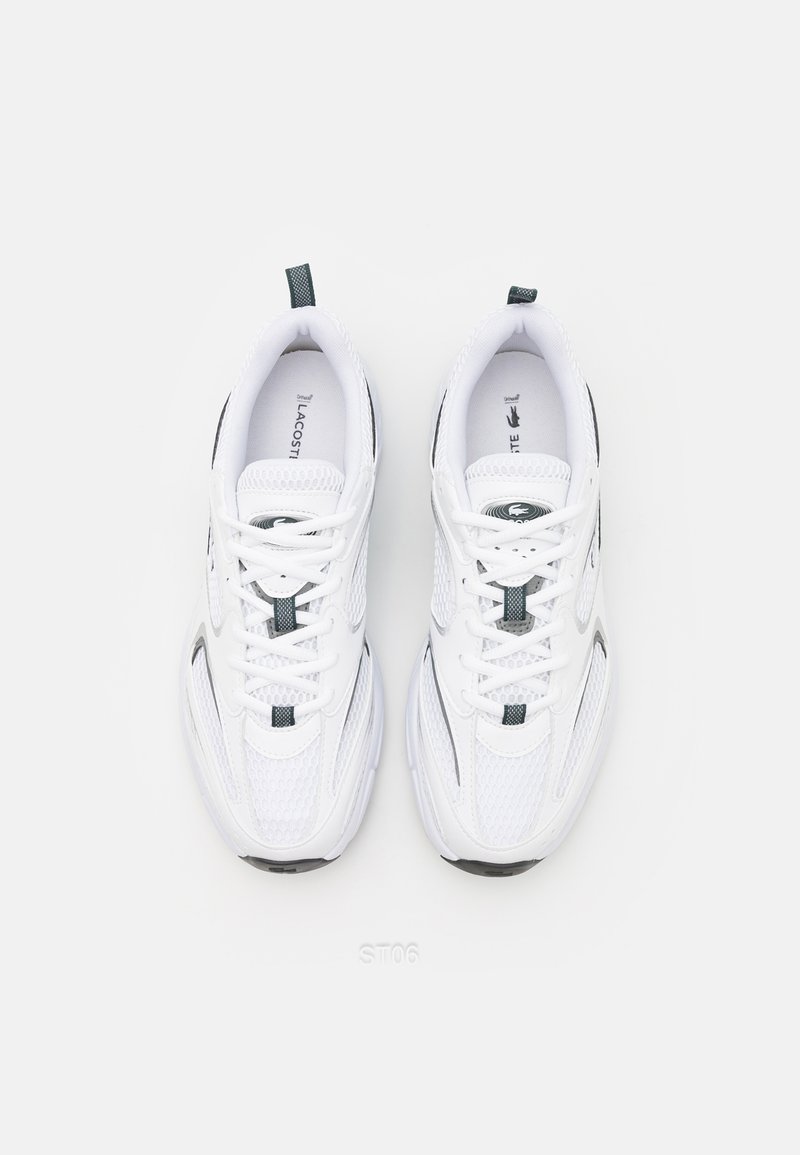 Sneakers da atletica bianchi con pannelli in rete, accenti grigi e una suola spessa. Presentano lacci e un logo di marca sulla linguetta.