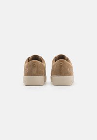 Sandfarbene Wildledersneaker mit durchbrochenem Design, beiger Gummisohle und goldenen Logoakzenten an der Ferse. Verjüngte Rückseite mit abgerundeten Kanten.