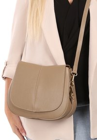 Beige schoudertas van textuurleer, met een klep-sluiting, verstelbare strap en subtiele gouden hardware accenten.