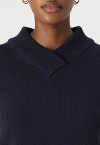 Pull en maille bleu marine avec un col en v côtelé et un tissu texturé, présentant une vue rapprochée de l'encolure.