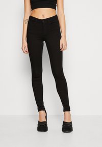 Pantalones vaqueros skinny negros hechos de tela elástica, con un diseño clásico de cinco bolsillos, cierre de botón en la parte frontal y un ajuste ceñido a lo largo de las piernas.
