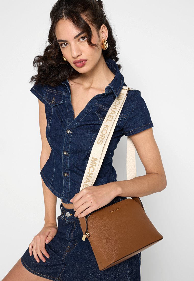 Sac à main en cuir marron au fini lisse, avec une fermeture éclair dorée et un logo, complété par une sangle beige portant le nom de marque imprimé.