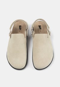 Cizme din suede bej, cu spatele închis, cu o textură netedă, talpă plată și curea ajustabilă cu închidere tip buton. Interiorul prezintă o branșă cu logo.