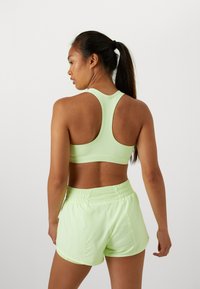 Débardeur athlétique vert clair avec un design dos nageur, accompagné de shorts légers assortis. Le tissu semble lisse et extensible.