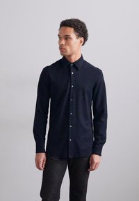Camicia a maniche lunghe blu navy con sottili strisce orizzontali, colletto a camicia e bottoni coordinati. Vestibilità slim, realizzata in tessuto testurizzato.