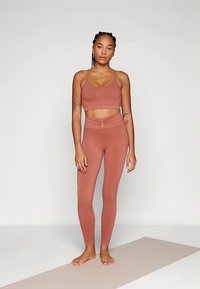 Kevyt, ruosteenvärinen urheiluliivi- ja legginssipaketti, jossa on istuva malli ja sileä pinta, keskikorkea vyötärönauha ja vähäiset saumadetaljit.