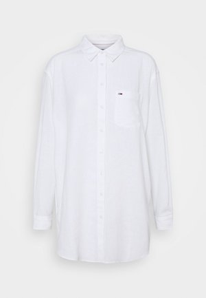 White long-sleeve button-up shirt with a collar and chest pocket featuring a small red, white, and blue logo on a plain background.