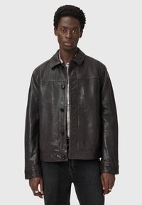 Veste en cuir brun foncé avec une surface légèrement texturée, dotée d'un col pointu, de boutons à l'avant et de deux poches poitrine.