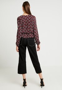 Blusa a manica lunga con un motivo a cuori rosse e bianche su uno sfondo nero; abbinata a jeans neri cropped a vita alta e sandali neri con tacco.
