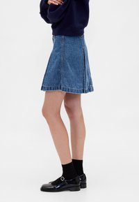 Denim A-lijn rok in middelblauw, met een rafelige zoom, een zijsplit en een getailleerde taille. Gecombineerd met zwarte Mary Jane schoenen en sokken.