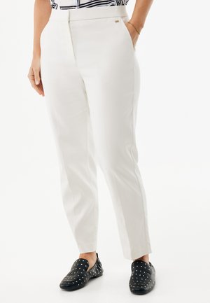 Pantalon blanc sur mesure avec une texture lisse, doté de poches latérales et d'un petit logo en accent, associé à des chaussures noires à enfiler ornées de clous.