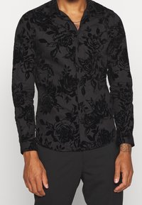 Zwarte langwerpige shirt met lange mouwen in een bloemenvelours patroon, met een slim fit, knoopsluiting aan de voorkant en een klassieke kraag.