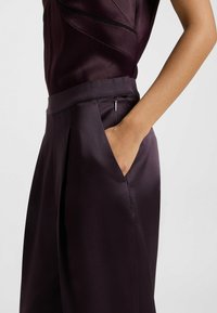 Donkerpaarse satijnen broek met een platte tailleband, zijzak en geplooide details, die een gladde textuur en een gestroomlijnd ontwerp laat zien.