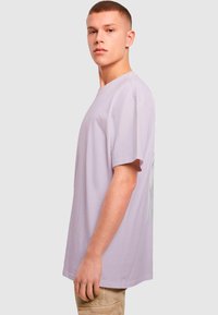 Lyse lilla bomulds t-shirt med korte ærmer, rund halsudskæring og sølv grafisk detalje på brystet. Casual pasform, glat tekstur.