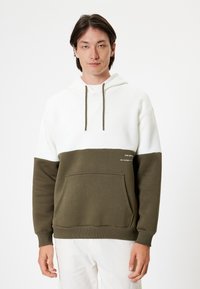 Hoodie med vita och olivgröna paneler. Har en känguruficka, ribbade ärmslut och en textdetalj på den nedre olivgrön delen.