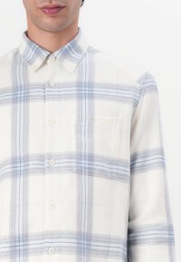 Wit en lichtblauw geruit overhemd met een button-down kraag, voorzien van een voorzak en een zachte textuur. De knopen zijn licht van kleur en rond.