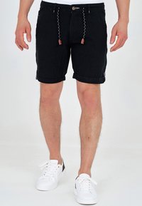 Shorts en jean noir avec ourlets retroussés, poches avant et fermeture à cordon avec détails en cuir marron. Associés à des baskets blanches.