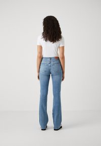 Svetlo modri razširjeni traperji s srednjim pasom, z rjavim usnjenim oznako in dvojno zadnjo žepno. Gladka denim tekstura. Nošena bela majica.