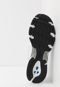 Svart gummisula med mönstrat mönster, vit mellansula, grå accenter och blå detaljer. Har rundad häl och design för stöd under fotvalvet.