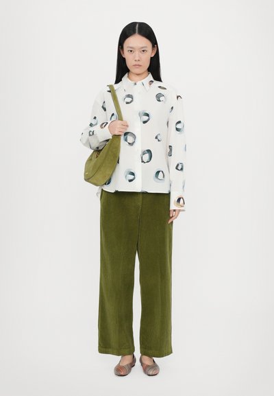 Camisa blanca con patrones circulares, pantalones de pana verde de pierna ancha, bolso de hombro verde y zapatos a rayas de múltiples colores. Texturas suaves.
