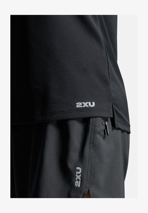 Zwart atletisch shirt met gestructureerde stof; heeft een klein wit "2XU" logo aan de zoom. Gecombineerd met zwarte shorts, ook met "2XU" branding.