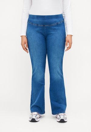 Blue denim flared jeans with a wide waistband, prominent stitching details, and a smooth texture. Paired with white sneakers.