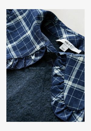 Sötét texturált anyagon navy kockás gallér fodros részlettel, "NEXT" felirattal. A gallér fehér csíkokkal díszített kockás mintázatú.