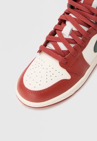 Czerwono-białe skórzane sneakersy z perforowanym noskiem, grubymi czerwonymi sznurowadłami, zielonymi akcentami i teksturowaną podeszwą.