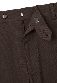 Pantaloni marroni a fantasia con chiusura a bottoni, cerniera e passanti per cintura. Presentano un dettaglio con linguetta per bretelle e una tasca laterale. Tessuto strutturato.