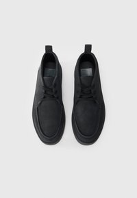 Chaussures en daim noir avec un bout arrondi, un design à lacets et une languette au talon. Surface texturée et détails de couture minimalistes.