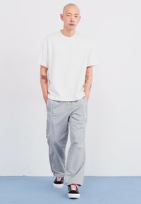 Witte t-shirt met korte mouwen, gecombineerd met lichtgrijze, losse broek met witte piping en zwarte sneakers met roze accenten.