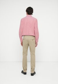 Man facing away wearing red and white striped long-sleeve shirt, beige trousers, and black shoes against a white background.