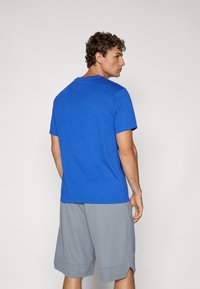 Tricou albastru din bumbac, cu guler rotund, mâneci scurte și o textură netedă, asociat cu pantaloni scurți gri, cu o croială ajustată și fante laterale.