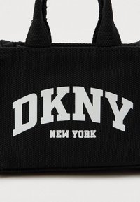Μαύρη ανάγλυφη τσάντα tote με λευκό τυπωμένο κείμενο "DKNY" και μικρότερο "NEW YORK" στο μπροστινό μέρος, με δύο ανθεκτικές λαβές.