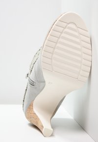 Gray suede high-heeled shoe featuring a cork wedge and a textured design. Smooth, light rubber sole with horizontal grooves for traction.