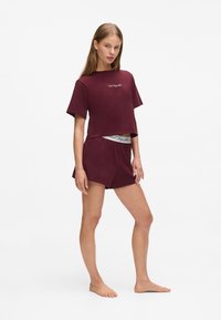 Bordeaux kort T-shirt met korte mouwen en bijpassende shorts, voorzien van een decoratieve tailleband met logo tekst, gemaakt van zachte stof.