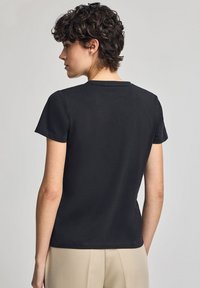 Czarny t-shirt krótki rękaw z okrągłym dekoltem, gładka bawełniana tekstura i proste wykończenie; widoczne szwy wzdłuż krawędzi.