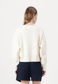 Krémový svetr s žebrovaným lemem a manžetami, volného střihu a s kleslými rameny, doplněný o námořnické šortky. Minimalistický design.