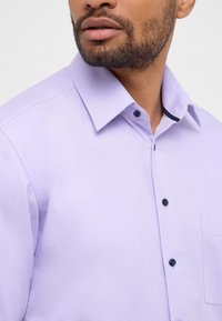 Camicia button-up di un leggero color viola con un piccolo motivo a scacchi, caratterizzata da un colletto appuntito, collo interno a contrasto e una singola tasca sul petto.