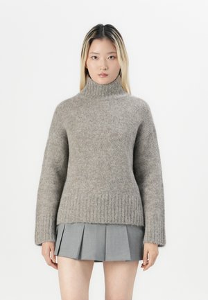 Helles graues Rollkragensweatshirt aus weicher Wolle mit gerippten Bündchen und Saum. Kombiniert mit einem grauen Faltenrock. Minimalistisches Design, glatte Textur.