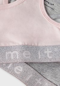 Light pink sports bra with a soft texture, featuring a wide silver elastic band with embossed text. Gray lining visible inside the band.